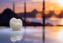 A photorealistic close-up of a flawless dental crown on a sterile surface. In the heavily blurred background, the sun rises over the Istanbul, Turkey skyline, creating a warm and inviting atmosphere.