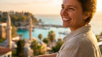 A close-up, side-profile shot of a person with a perfect, bright smile, standing on a balcony with a beautifully blurred background of a Turkish city and coastline at sunset.