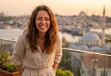 A happy woman with a perfect, bright smile stands on a sunny balcony, with the blurred skyline of Istanbul, Turkey, visible in the background, representing a successful dental tourism journey.