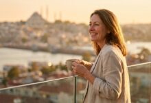A happy British woman with a perfect smile enjoys the sunrise from a balcony with a blurred view of Istanbul, symbolizing the positive experience of dental tourism.