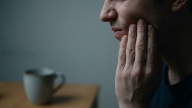 A photorealistic close-up of a person holding their jaw in pain, symbolizing the warning signs of a tooth infection. The lighting is dramatic and the background is blurred.
