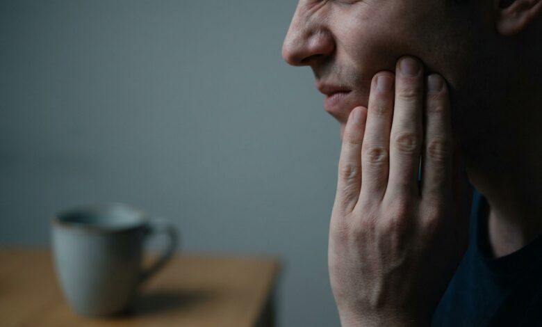 A photorealistic close-up of a person holding their jaw in pain, symbolizing the warning signs of a tooth infection. The lighting is dramatic and the background is blurred.