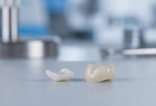 A close-up, photorealistic image showing a delicate porcelain dental veneer next to a robust Zirconium dental crown, displayed on a clean, modern surface, symbolizing the choice in cosmetic dentistry.
