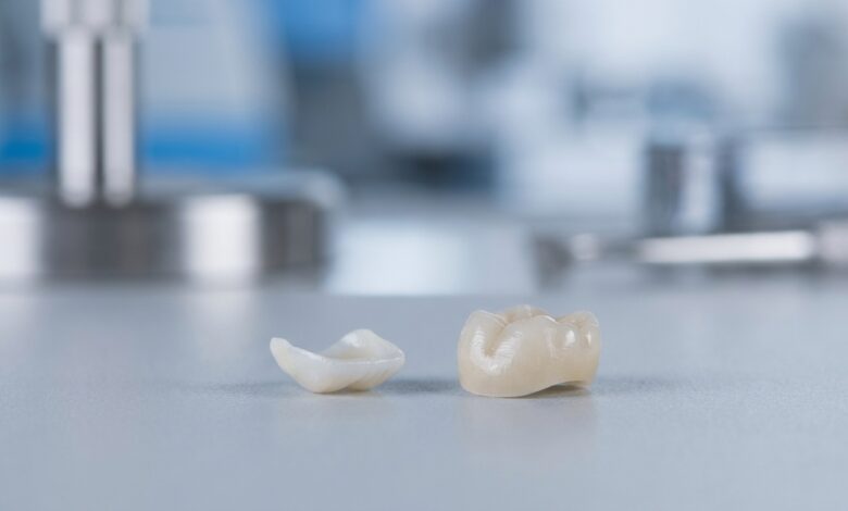A close-up, photorealistic image showing a delicate porcelain dental veneer next to a robust Zirconium dental crown, displayed on a clean, modern surface, symbolizing the choice in cosmetic dentistry.