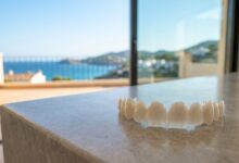 A close-up shot of flawless white dental veneers, with the beautiful, sunny, and blurred coastline of Turkey visible in the background, representing a dental holiday.