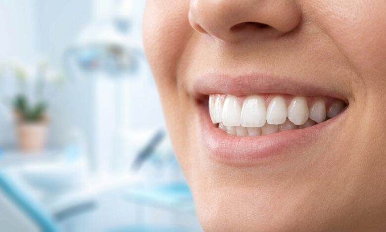 A detailed, photorealistic close-up of a person's incredibly bright, white, and healthy smile. The background is a softly blurred, modern, and clean professional setting.
