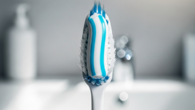 A photorealistic close-up of a soft-bristled toothbrush with a stripe of specialized white and blue sensitive toothpaste, against a softly blurred background of a clean bathroom counter.