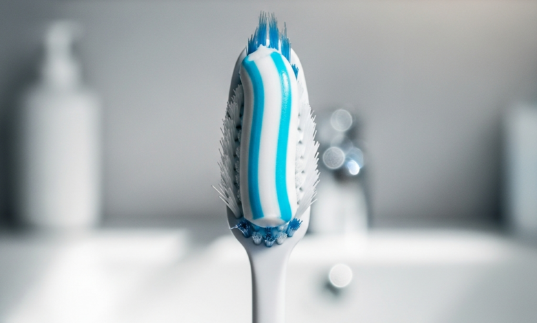 A photorealistic close-up of a soft-bristled toothbrush with a stripe of specialized white and blue sensitive toothpaste, against a softly blurred background of a clean bathroom counter.