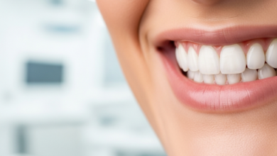 Close-up of a person smiling broadly, revealing perfect, bright white, natural-looking teeth, suggesting the results of dental veneers. The background is a soft, blurred image of a clean, modern dental office.