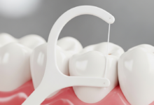 Close-up macro shot of healthy teeth and pink gums with a white dental floss strand gently positioned in the interdental space, demonstrating effective oral hygiene. The background is softly blurred.