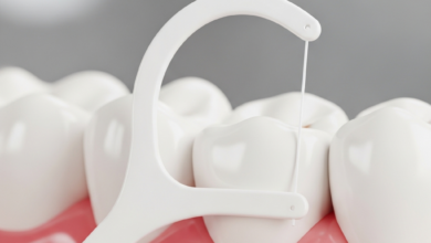 Close-up macro shot of healthy teeth and pink gums with a white dental floss strand gently positioned in the interdental space, demonstrating effective oral hygiene. The background is softly blurred.