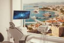 A modern, bright dental clinic interior with a contemporary dental chair and sleek equipment in the foreground. Through a large, soft-focus window in the background, a sunlit Turkish coastal city with traditional buildings and blue sea is visible under a clear sky. The image combines themes of dental care and travel.
