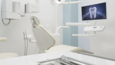 A clean, brightly lit modern dental examination room with a white dental chair, an overhead operating light, and blurred dental instruments on a tray in the foreground. Advanced, sleek dental equipment is visible in the background, conveying a sense of high quality and professionalism.