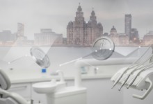 A soft focus image featuring the iconic Liver Building and Liverpool waterfront blurred in the background, with a clean, sterile dental clinic environment in the foreground. Abstract metallic shapes, resembling polished coins or geometric patterns, are subtly integrated, symbolizing the financial aspects of dental care.