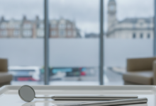 Close-up of clean, sterile dental instruments, including a mirror and a probe, resting on a white tray in a bright and modern dental clinic. The background is softly blurred, showing a subtle urban landscape typical of the United Kingdom through large windows.